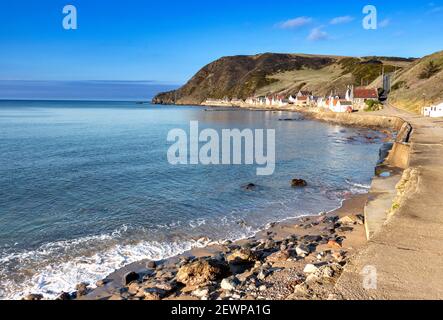 CROVIE VILLAGGIO ABERDEENSHIRE SCOZIA UNA FILA DI CASE LA PASSERELLA UN CIELO BLU E UN'ONDA CHE SI INFRANGONO SULLA SABBIA E SPIAGGIA DI CIOTTOLI Foto Stock