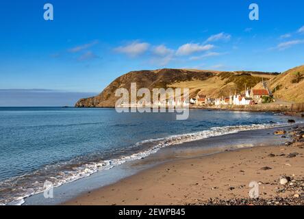 CROVIE VILLAGGIO ABERDEENSHIRE SCOZIA UNA FILA DI CASE CON ROSSO TEGOLE DEL TETTO UN CIELO BLU E UN'ONDA CHE SI INFRANA UNA PICCOLA SPIAGGIA DI SABBIA Foto Stock