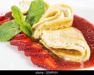 porzione di crepes con panna montata e fragole fresche con sciroppo su piastra bianca Foto Stock