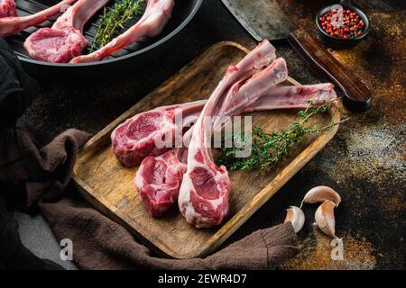 Costolette di agnello crude o tagli di montone, con ingredienti, su padella in ghisa, su vecchio sfondo rustico scuro Foto Stock