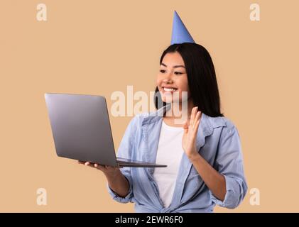 Allegra donna asiatica in Hat che fa videocall su laptop Foto Stock