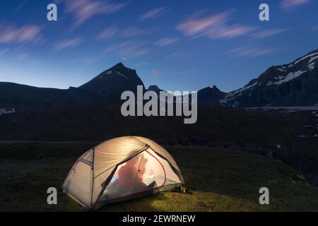 Silhouette di escursionista all'interno della tenda illuminata sopra il lago Limmernsee al tramonto, Canton Glarona, Svizzera, Europa Foto Stock