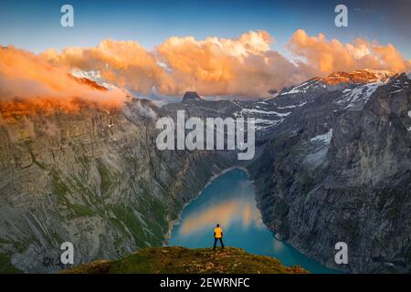 Uomo in piedi su rocce che guarda le nuvole al tramonto sul lago Limmernsee, vista aerea, Canton Glarona, Svizzera, Europa Foto Stock