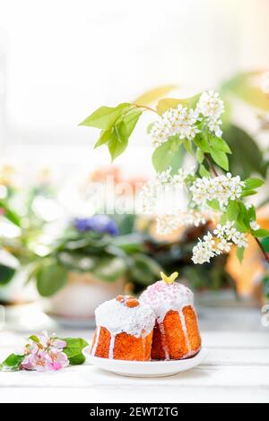 Due pane pasquale decorato su un piatto con fiori di mela. Sullo sfondo, piante e fiori. Orientamento verticale. Spazio di copia. Concetto di Pasqua Foto Stock