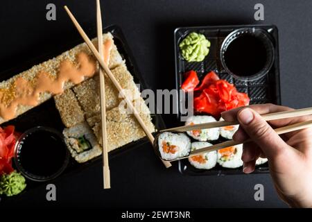 Pezzo di sushi con le mani della donna con bastoni da contenitore di plastica su sfondo nero. Foto Stock