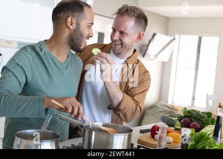 Multi etnica gay maschio coppia sorridente e preparare insieme il cibo a casa Foto Stock