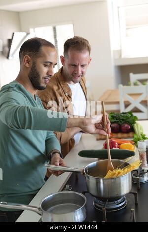 Multi etnica gay maschio coppia sorridente e preparare insieme il cibo a casa Foto Stock