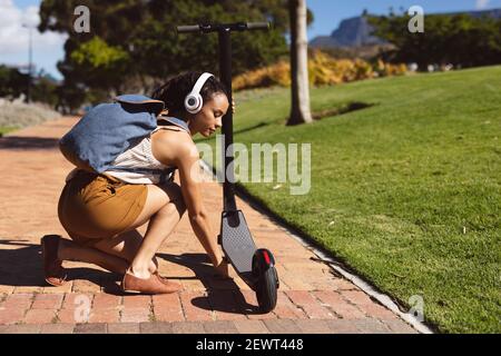 Donna afroamericana che indossa le cuffie parcheggia uno scooter in strada Foto Stock