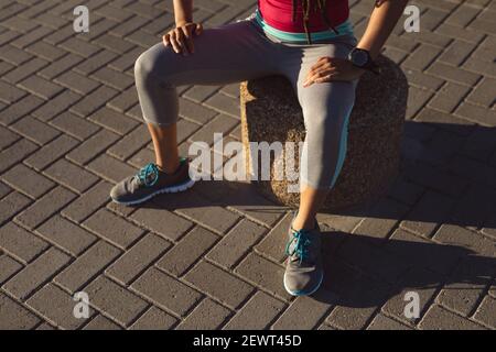 Sezione centrale della donna afroamericana che si prende pausa in esercizio su una passeggiata sul mare, seduto Foto Stock