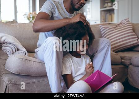 L'uomo afroamericano seduto sul letto facendo i capelli della figlia Foto Stock