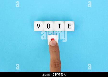 La parola voto scritto su cubi di legno con una mano maschio che preme il pulsante di votazione. Concetto di voto online in politica o incontri di affari. Foto Stock