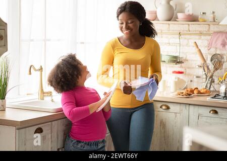 Little Black Girl strofinare i piatti insieme alla mamma in cucina Foto Stock