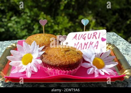 Piccolo vassoio composto da 3 muffin con scaglie di cioccolato, un regalo per la festa della mamma, con margherite e chuoricini e una carta che dice "Happy Mother's Day" in me Foto Stock