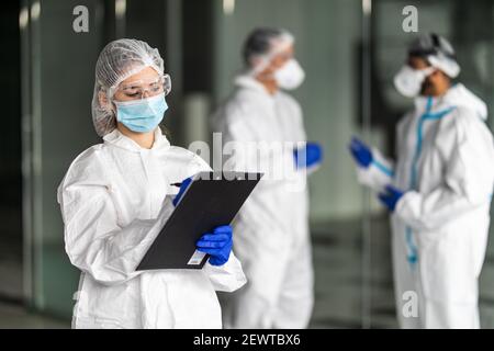 Operatori sanitari operatori sanitari che indossano tute nocciole che lavorano insieme a. controllare un focolaio di virus Foto Stock