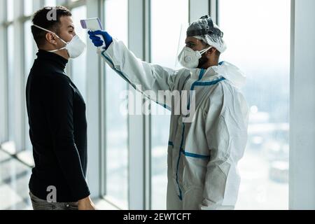 Il personale dell'ufficio medico ha utilizzato il termometro digitale per Misurare la temperatura del visitatore femminile al building.Measures a. prevenire le persone con Foto Stock