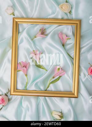 Cornice dorata in cima al raso blu con rose e fiori rosa primavera. Concetto di molla piatta. Foto Stock
