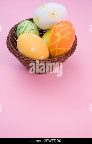 Uova di Pasqua colorate nel cestino sullo sfondo rosa con uno spazio per la copia Foto Stock