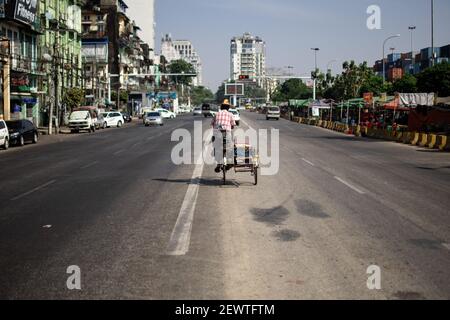 YANGON, MYANMAR - 1 GENNAIO 2020: Un uomo locale birmano in longyi tradizionale fa una bicicletta in mezzo alla strada nel traffico una giornata calda Foto Stock