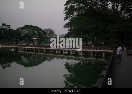 YANGON, MYANMAR - 1 GENNAIO 2020: Il lago Kandawgyi riflette un ponte a piedi e il lussureggiante parco verde con i suoi alberi in acqua durante la sera Foto Stock