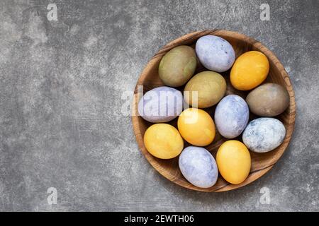 Uova di Pasqua su piastra di legno verniciata con coloranti naturali. Vista dall'alto, primo piano. Foto Stock