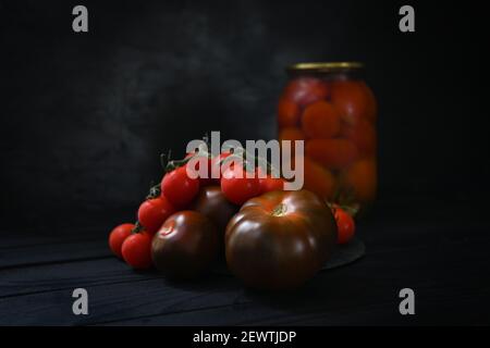 Gustose conserve di pomodori fatti in casa in vasetto di vetro. Pomodori freschi e in scatola su sfondo nero. Foto Stock