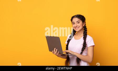 Giovane donna indiana sicura che tiene e usa il computer portatile Foto Stock