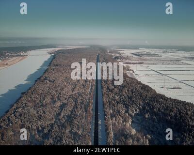 Tortuosa strada asfaltata tra alberi innevati in foresta creando tunnel in un paesaggio nebbioso. Guida su strada. Przywidz, Kashubia, Polonia Foto Stock