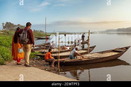 Coppia turistica in attesa di un giro in barca sul fiume al tramonto in un villaggio nel Bengala Occidentale, India Foto Stock