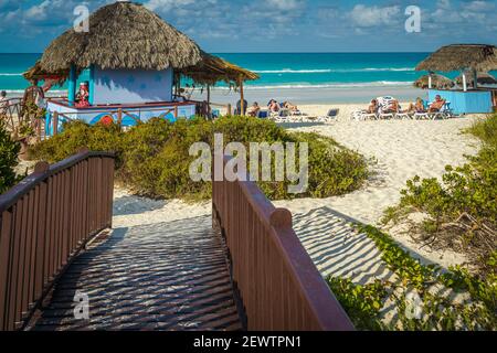 Cayo Santa Maria, Cuba, 2016 febbraio - Boardwalk per la spiaggia esotica con i vacanzieri prendere il sole intorno ripari paglia Foto Stock