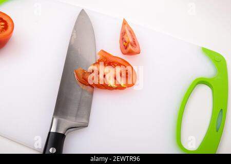 Su un tagliere c'è un pomodoro fresco tagliato rosso e un grande coltello da chef. Su uno sfondo bianco isolato. Foto Stock