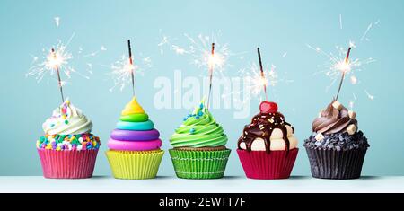 Assortimento di cupcakes celebrativi dai colori vivaci decorati con scintillatori per una festa di compleanno Foto Stock