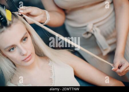 Parrucchiere femmina che fa estensioni di capelli a giovane donna con capelli biondi in salone di bellezza. Prolunga professionale per capelli Foto Stock