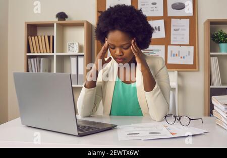 Donna millennial afro-americana overworked che sente forte mal di testa siedono davanti di computer portatile Foto Stock