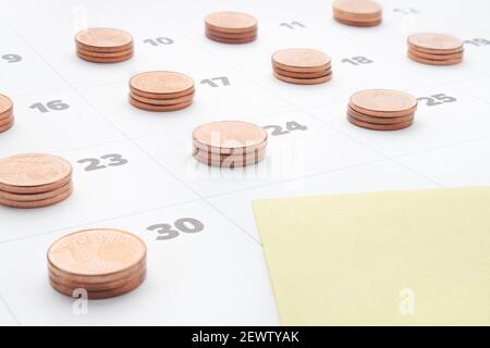 Pianificare risparmiare denaro per la gestione del budget. Costo della vita. Rapporto mensile. Nota di carta gialla vuota nel calendario dell'ultimo giorno del mese con pile di monete in euro Foto Stock