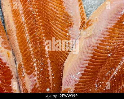 Primo piano di filetto fresco di pesce crudo in pezzi di ghiaccio. Pesce fresco sdraiato sul banco del supermercato con ghiaccio trasparente schiacciato. Salmone. Foto Stock