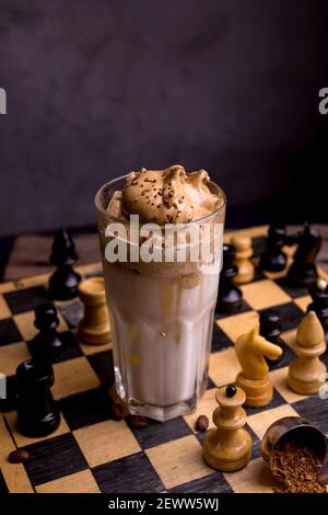 Caffè Dalgona. Bevanda ghiacciata montata con caffè istantaneo popolare in Corea cocktail cremoso in bicchieri alti decorati con scacchi su scacchiera di legno Foto Stock