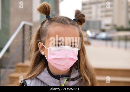 Bambina 9s piccola seria con doppio grappolo corna acconciatura in maschera rosa monouso in piedi da solo all'aperto. Covid-19 pandemia epidemia mondiale, tutti Foto Stock