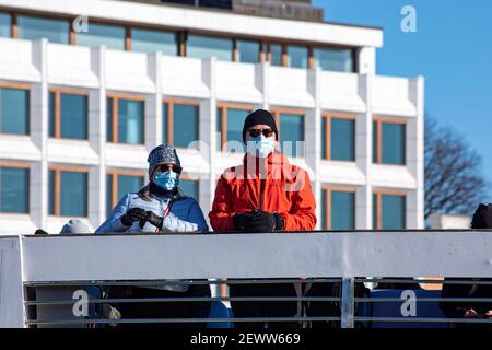 Maschera che indossa una coppia sul ponte dei traghetti Suomenlinna con l'ex quartier generale Enso-Gutzeit sullo sfondo a Helsinki, Finlandia Foto Stock