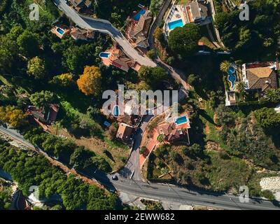 Direttamente dall'alto verso ville di lusso con piscine, strade e vegetazione lussureggiante durante il giorno di sole. Quartiere spagnolo residenziale dis Foto Stock