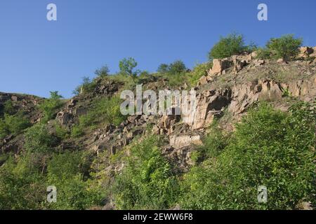 Un pendio roccioso di una cava di granito abbandonata nella regione di Nikolaev in Ucraina in una calda giornata estiva. Pietre affilate sopravite con vegetazione sparsa. Blu Foto Stock