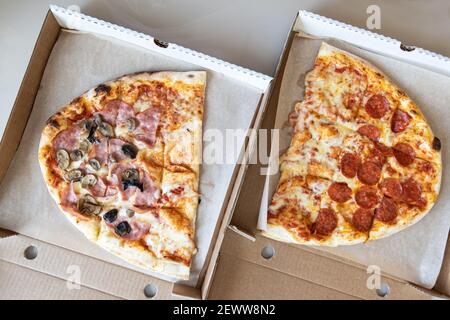 La pizza di famiglia, ovale, divisa in due metà, è composta da tre tipi: margarita, pepperoni, funghi prosciutto. Concetto di consegna di cibo, da asporto, italiano Foto Stock