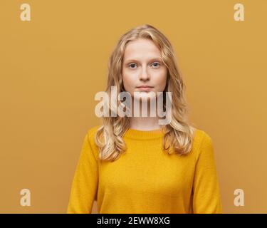 Vita in su ritratto di bella giovane bionda seria intelligente scandinava donna su parete arancione giallo brillante Foto Stock