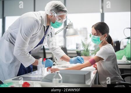 In una clinica privata infermiere un uomo mette un tourniquet sul braccio di una paziente femmina e prende il sangue da una vena per l'analisi Foto Stock