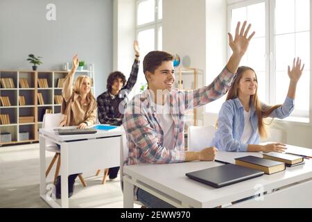 Gruppo di studenti delle scuole superiori o universitari che alzano le mani seduti alle scrivanie in classe Foto Stock