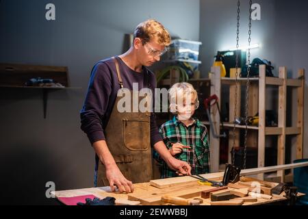un falegname esperto mostra il lavoro di vari attrezzi a suo figlio in officina. Foto Stock