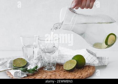 Disintossicare l'acqua con la frutta di lime. Versate a mano l'acqua di lime dalla caraffa nei bicchieri Foto Stock