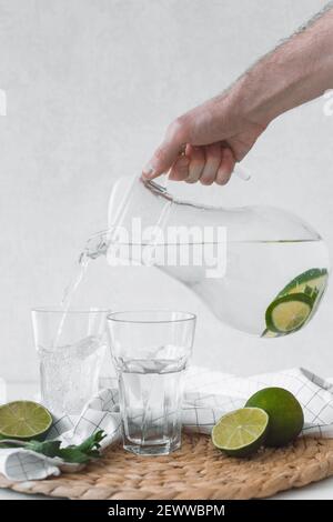 Disintossicare l'acqua con la frutta di lime. Versate a mano l'acqua di lime dalla caraffa nei bicchieri Foto Stock