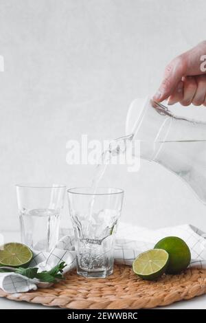 Disintossicare l'acqua con la frutta di lime. Versate a mano l'acqua di lime dalla caraffa nei bicchieri Foto Stock