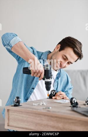 Il trapano elettrico funziona nelle mani di handyman, assembla e ripara i mobili a casa Foto Stock