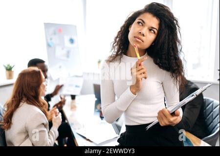 Ritratto di donna afroamericana pensiva. Pensare giovane donna di affari sembra pensieroso via, thik circa strategia o idea, in background sono i suoi colleghi Foto Stock